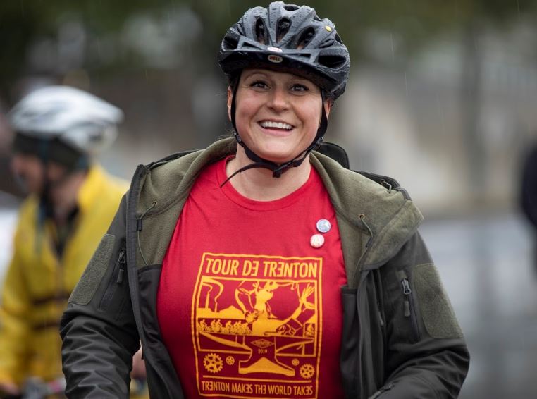 Photo of smiling woman with red "Tour de Trenton" shirt and bike helmet.