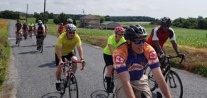a group of cyclists ride through a rural setting, toward the camera