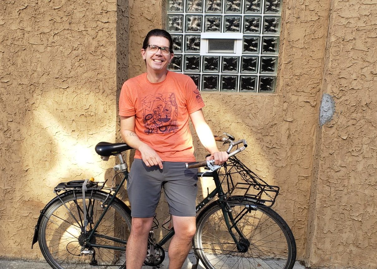 Leonard standing with his bike against a wall in the sunlight, wearing the famous Philly Pride bicycle coalition shirt