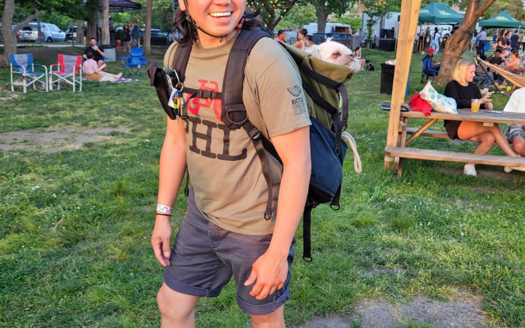 Transportation Community Organizer Lor Song smiling, wearing a helmet and a backpack with his puppy inside.