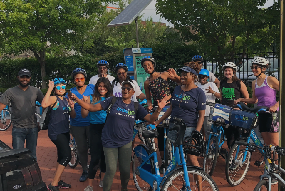 A group of bike riders pose in front of an Indego Bike Share station