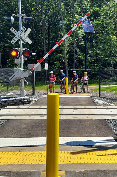 View of four people with bikes waiting to cross the railroad tracks on a new crossing of the Delaware Heritage Trail 
